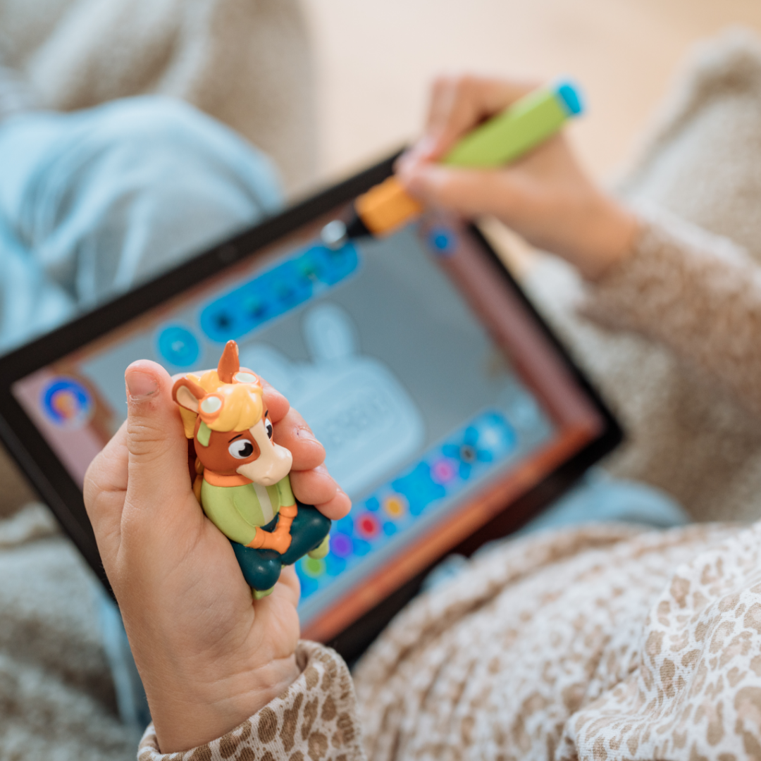 Ein Kind hält das Alex "Die Uhr lernen" Tierspielzeug von Edurino DE in der Hand und benutzt einen Stift auf einem Tablet mit einer bunten Zeichen-App.