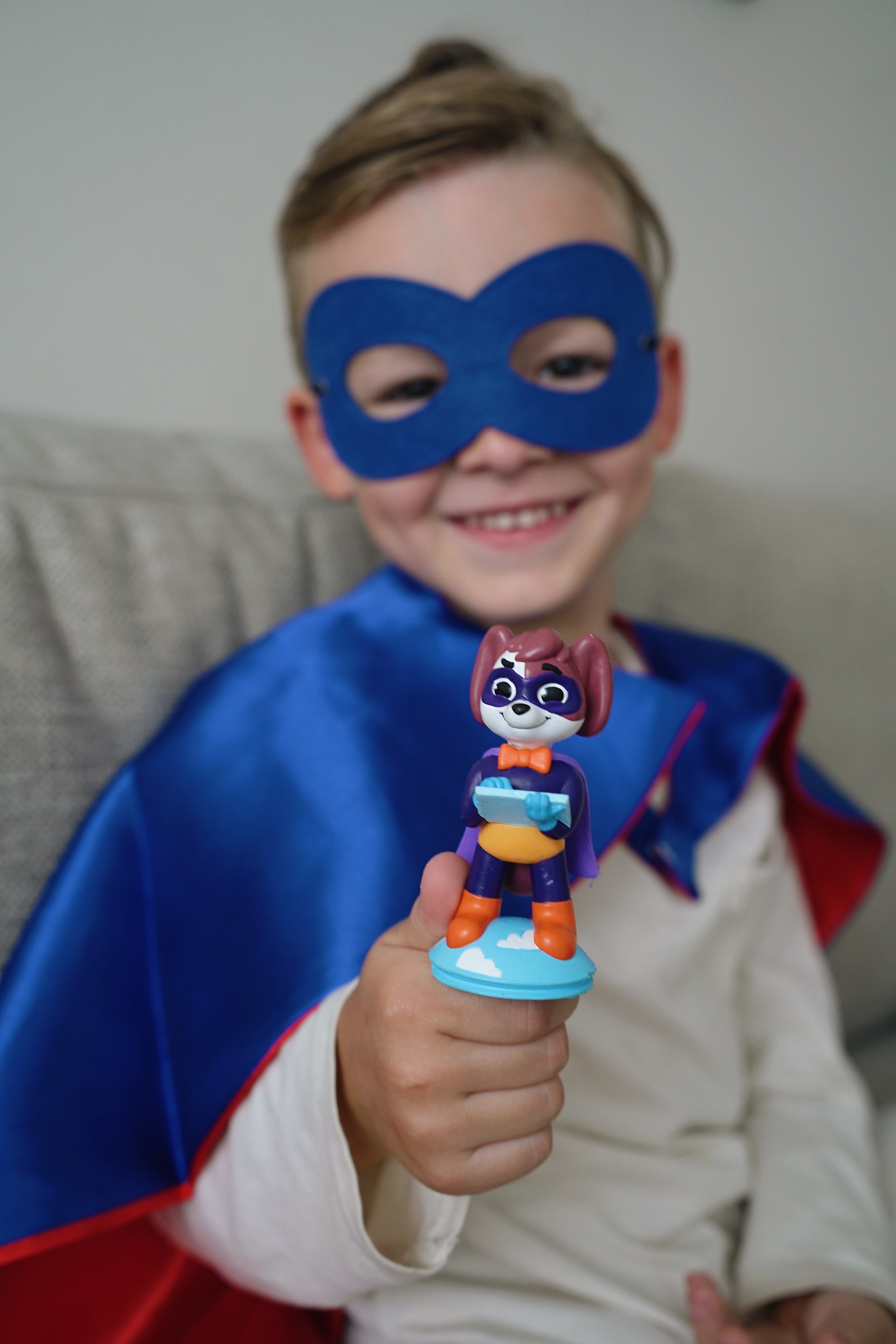 Ein Junge mit Superhelden Cape und Maske grinst und hält Luca in die Kamera