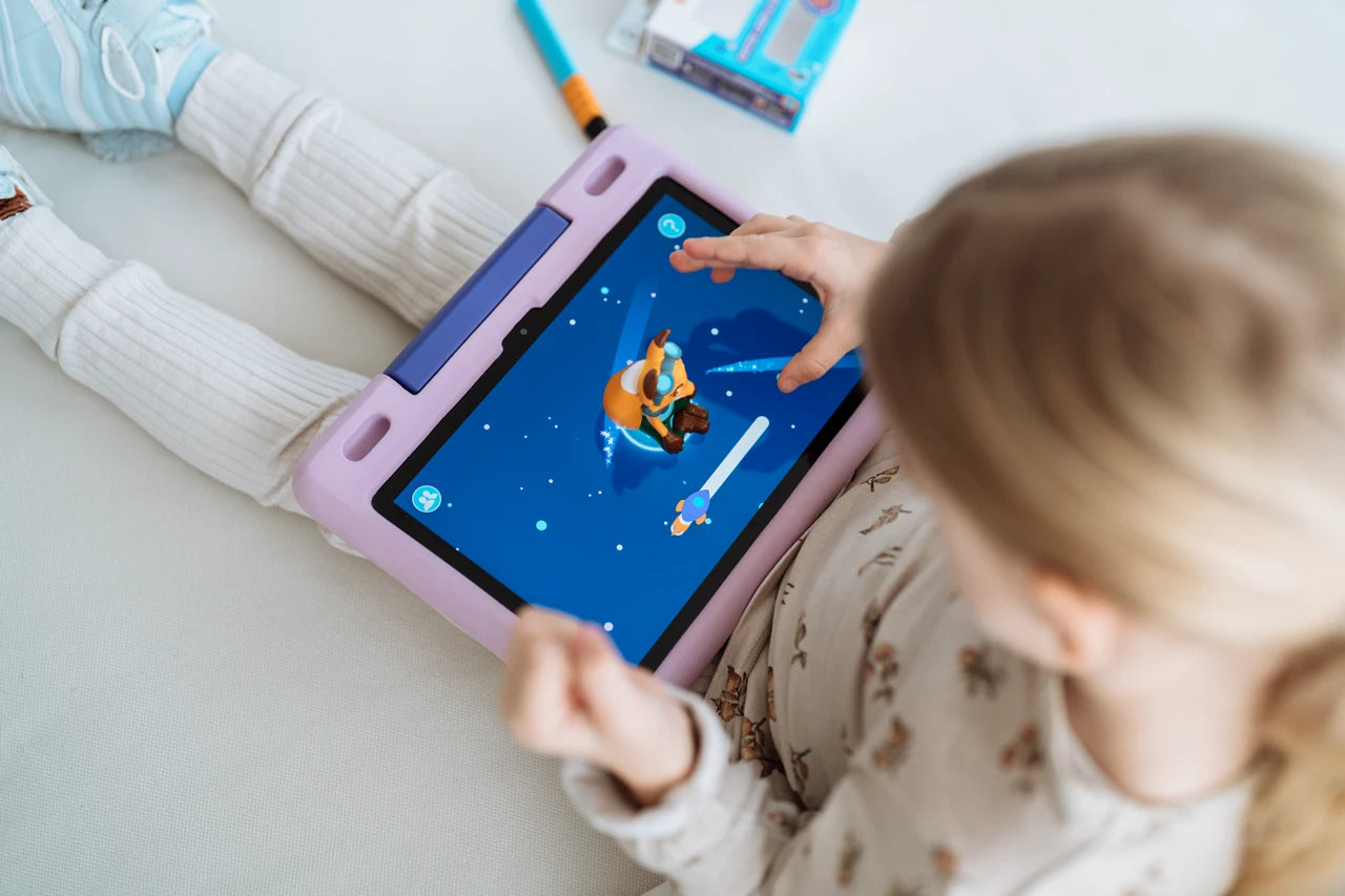 Kind spielt auf einem Bett sitzend ein Weltraumspiel auf einem Tablet.