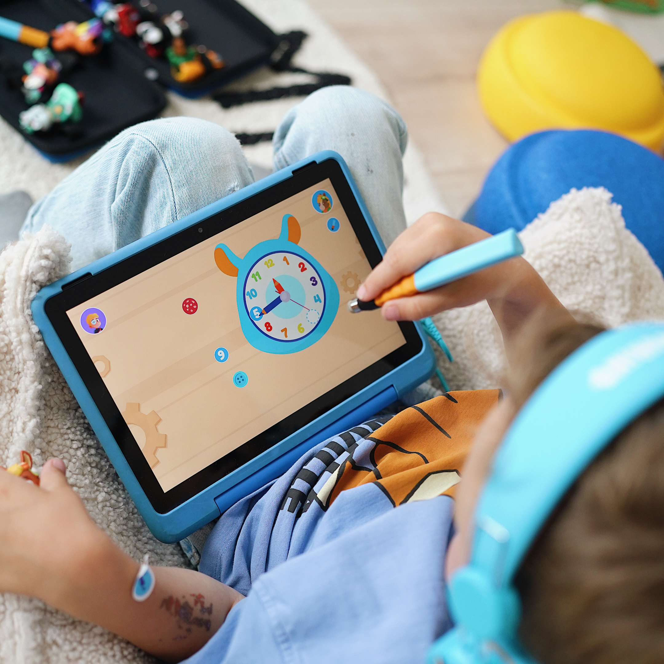 Ein Kind benutzt einen Stift, um ein Uhrenspiel auf einem Tablet zu spielen, während es blaue Kopfhörer trägt, die mit dem Edurino DE Basis Starter-Bundle ausgestattet sind.